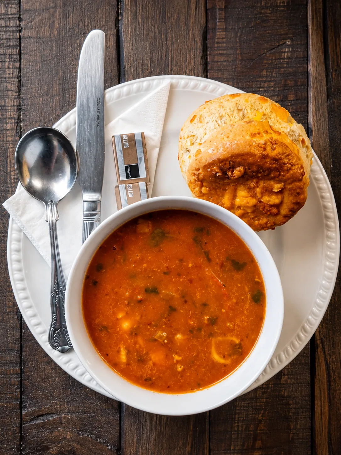 A bowl of soup with a cheese scone and butter