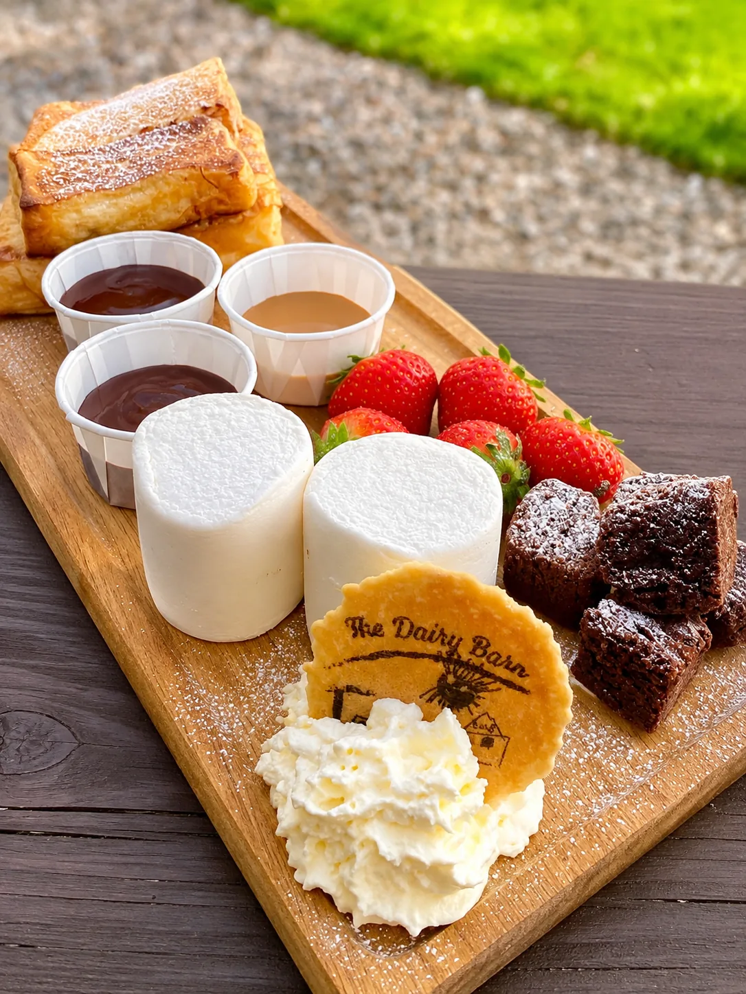 A dessert board with strawberries, brownies, sauces and whipped cream